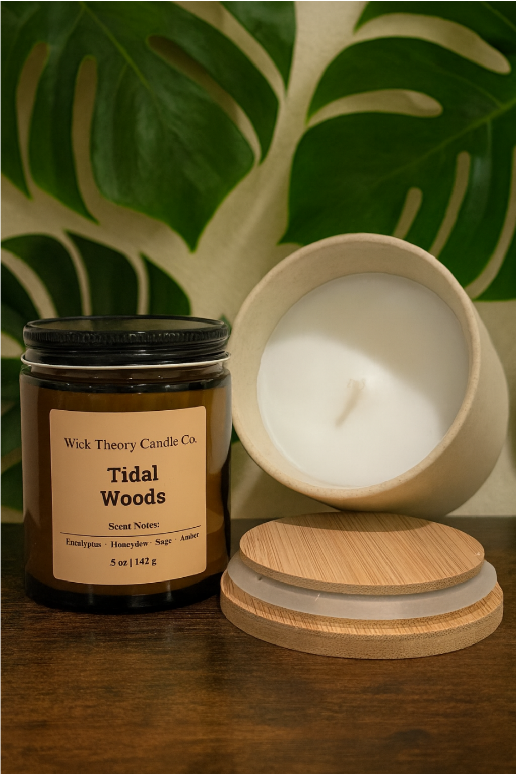 Wick Theory Candle Co. Tidal Woods  5 oz. glass candle and 10 oz. ceramic candle on a dark wooden surface with green mostera leaves in the background